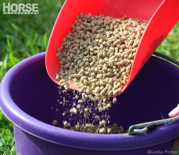 A horse feed scoop pouring pellets into a feeding bucket