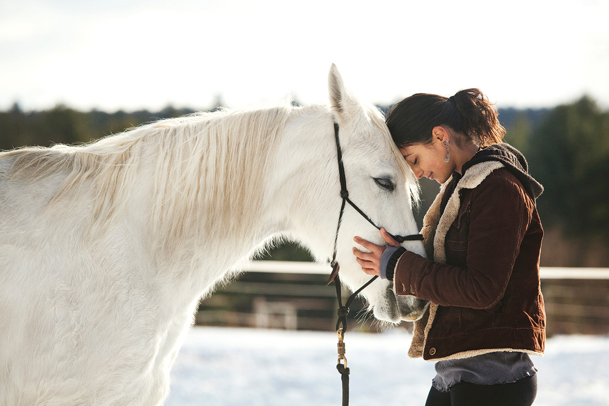 A woman hugging a gray mare in winter.