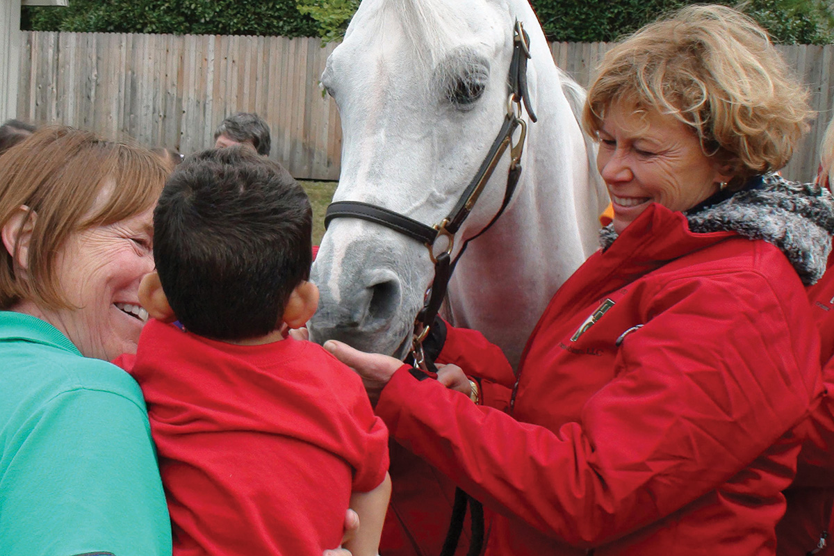 Mary Trowbridge, founder of the Arabian Horsemen’s Distress Fund, interacts with a horse and child