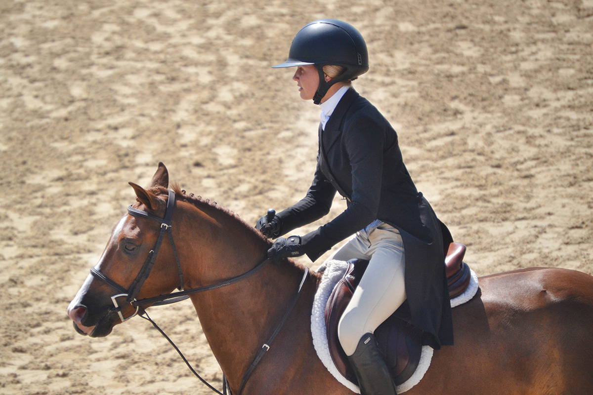 A girl riding a horse and wearing proper attire, including a riding helmet