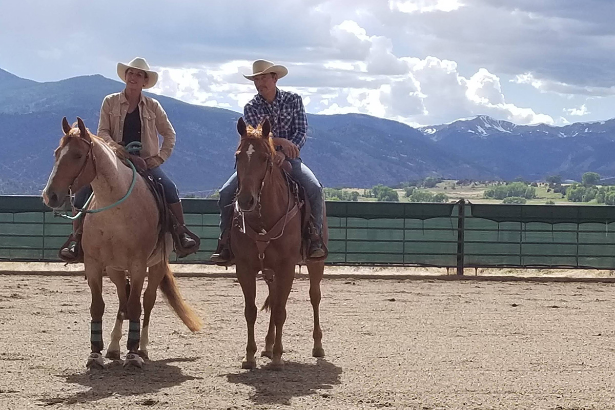 Julie Goodnight and her husband, Rich Moorhead, on horses with a mountain backdrop