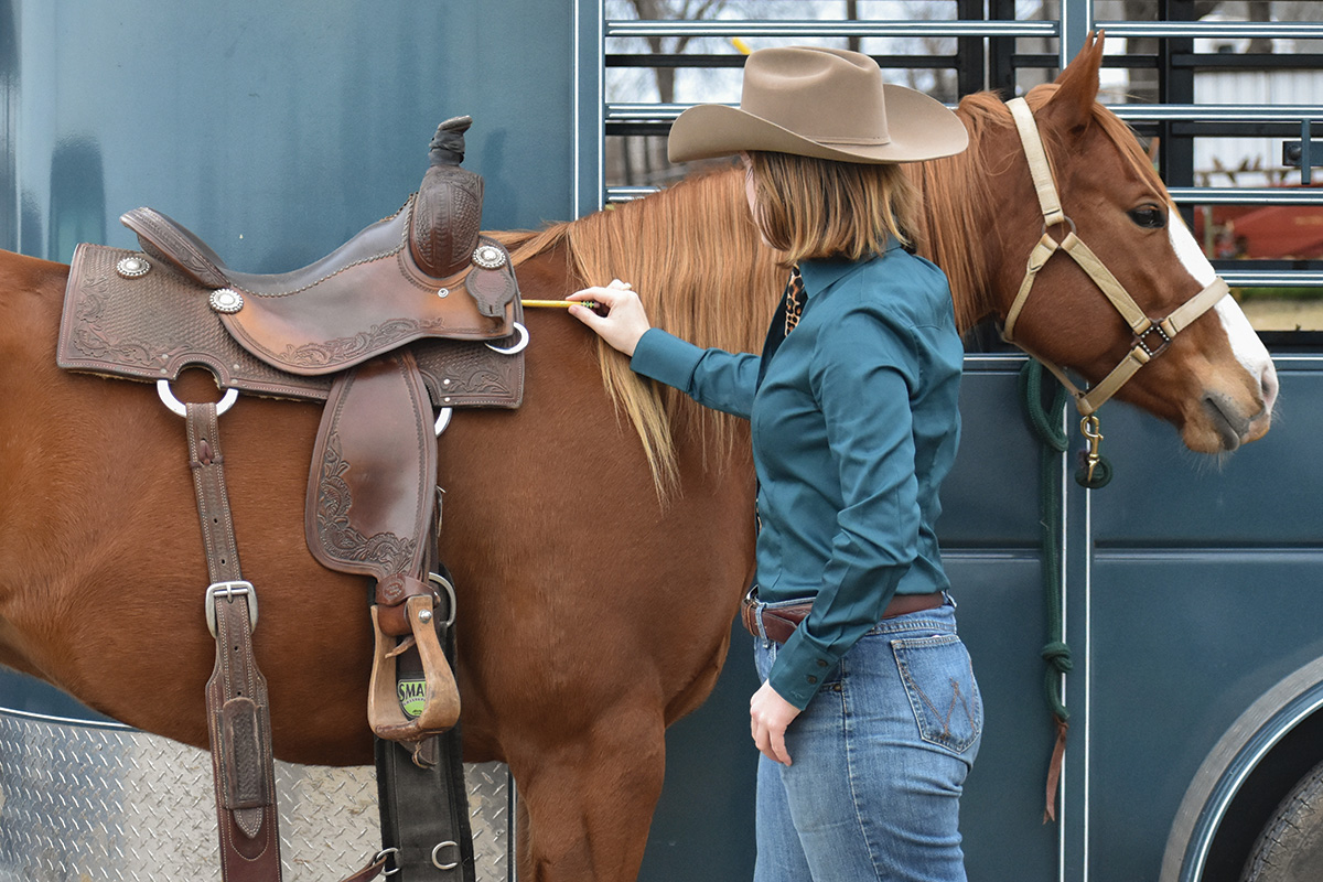 A cowgirl making sure her saddle is fitting her horse properly by using a pencil to measure the fit