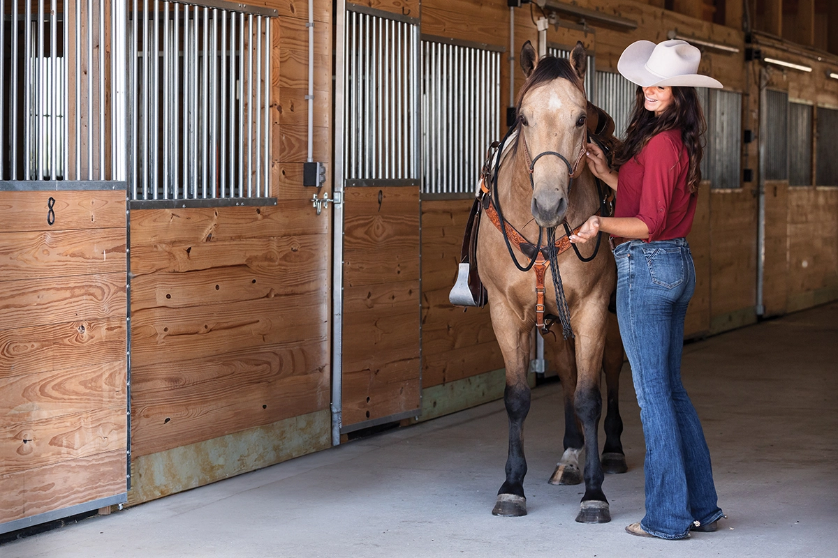 An equestrian in a barn with a buckskin horse.