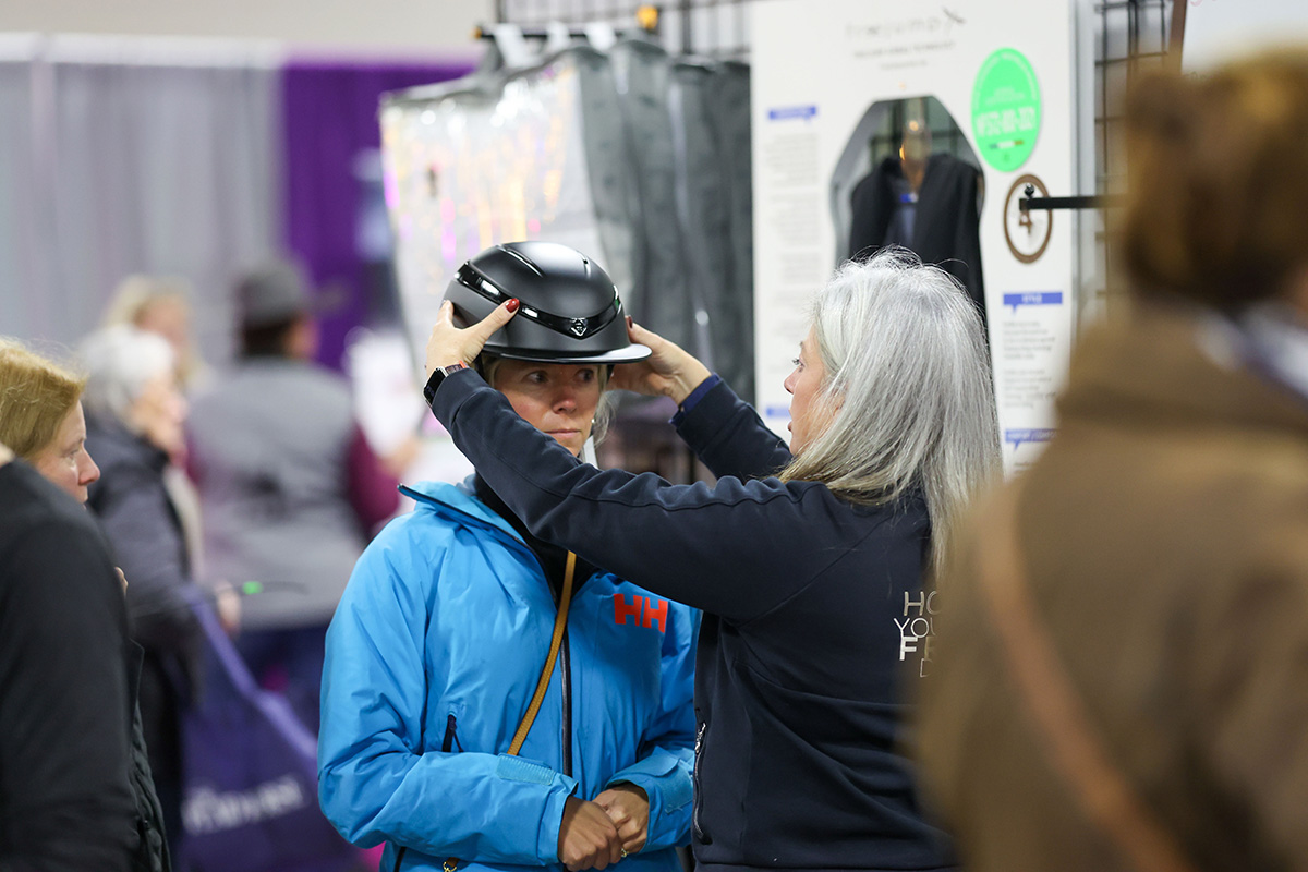 An equestrian shops for a new helmet and tries it on