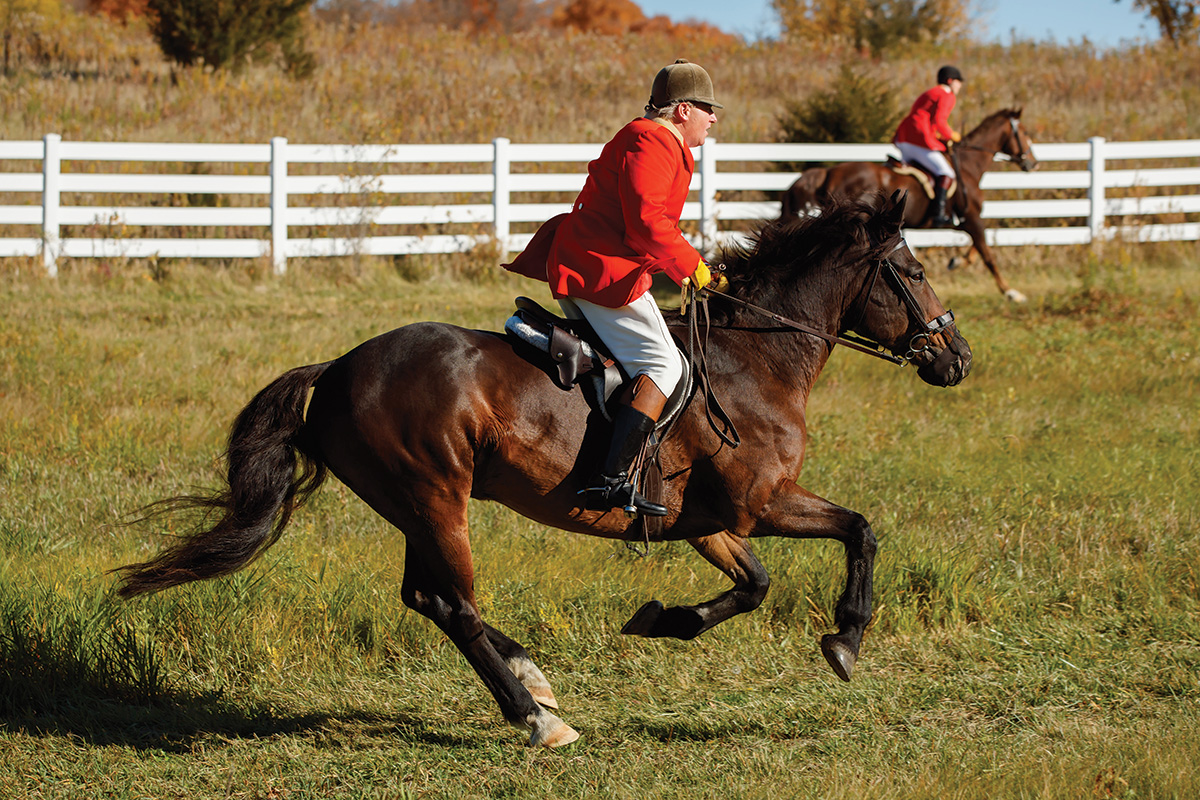 A staff member wears a traditional red coat while galloping his horse