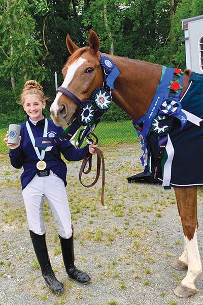 A young equestrian and her horse showing off their awards from a successful horse show