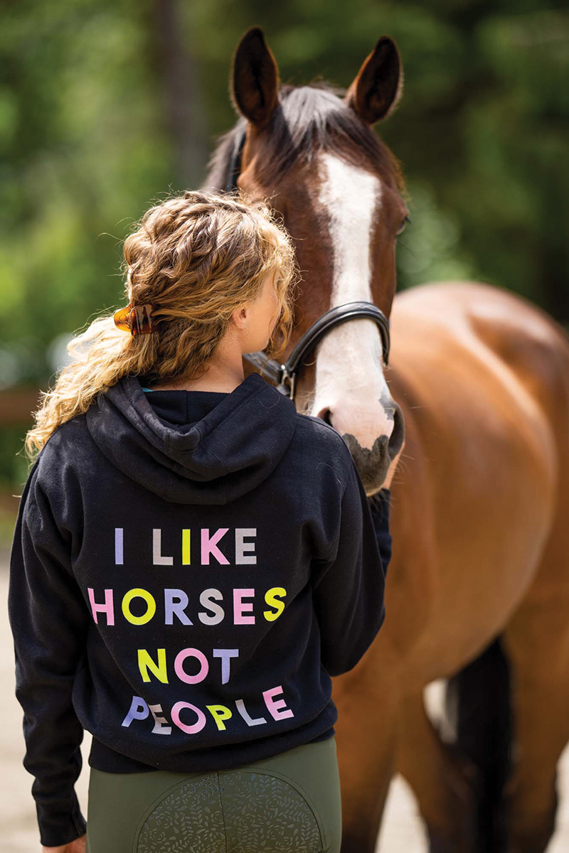 A sweatshirt from equestrian brand "I like horses, not people" worn by a girl with her horse