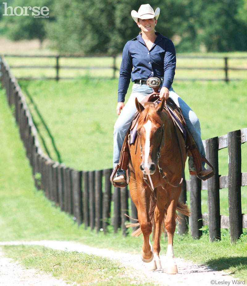 Western horse and rider riding along a fenceline