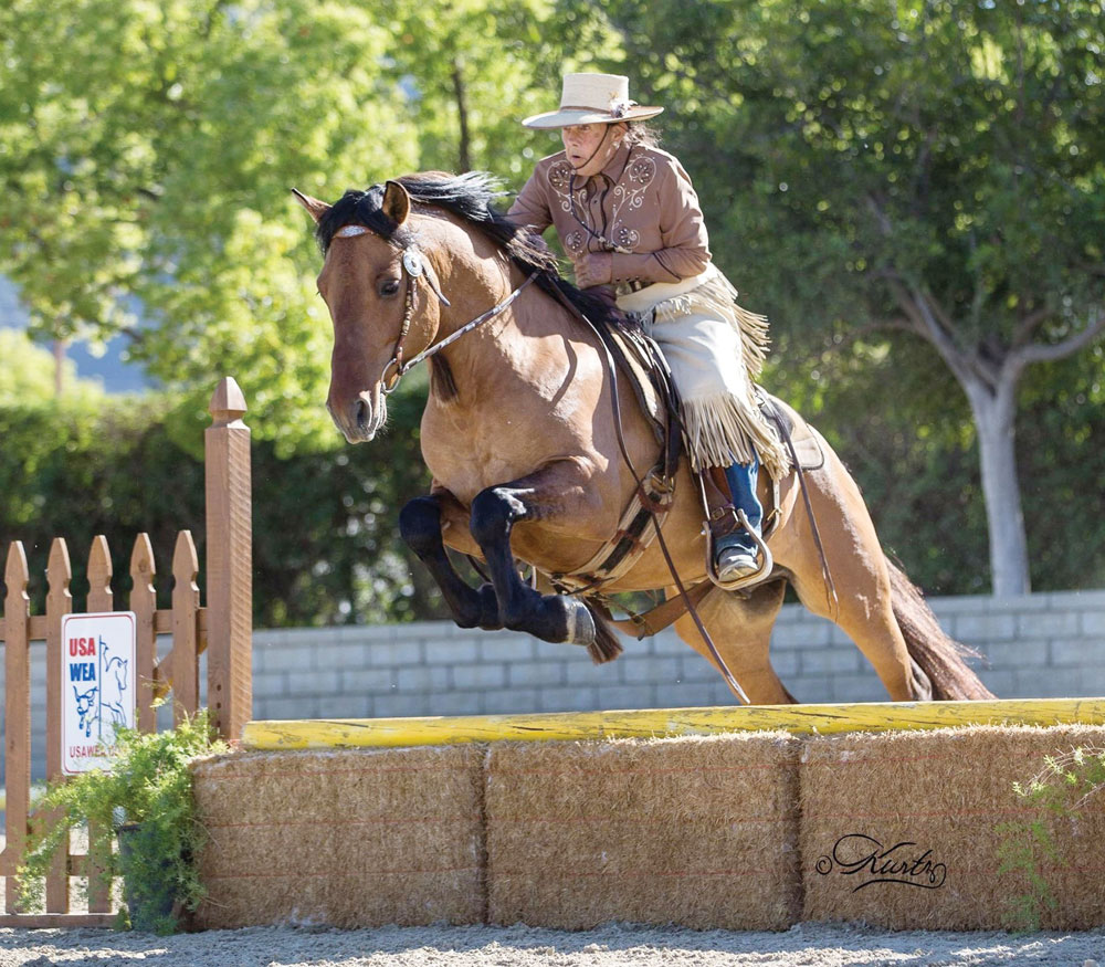 Working Equitation competitors jumping over straw bales