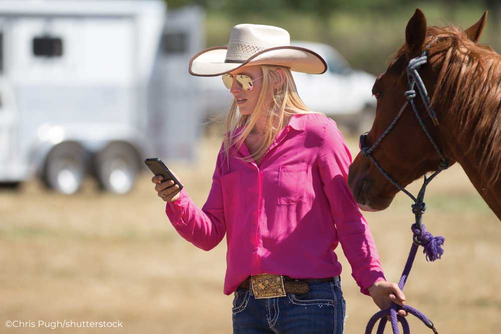 Western rider holding a horse and a mobile phone