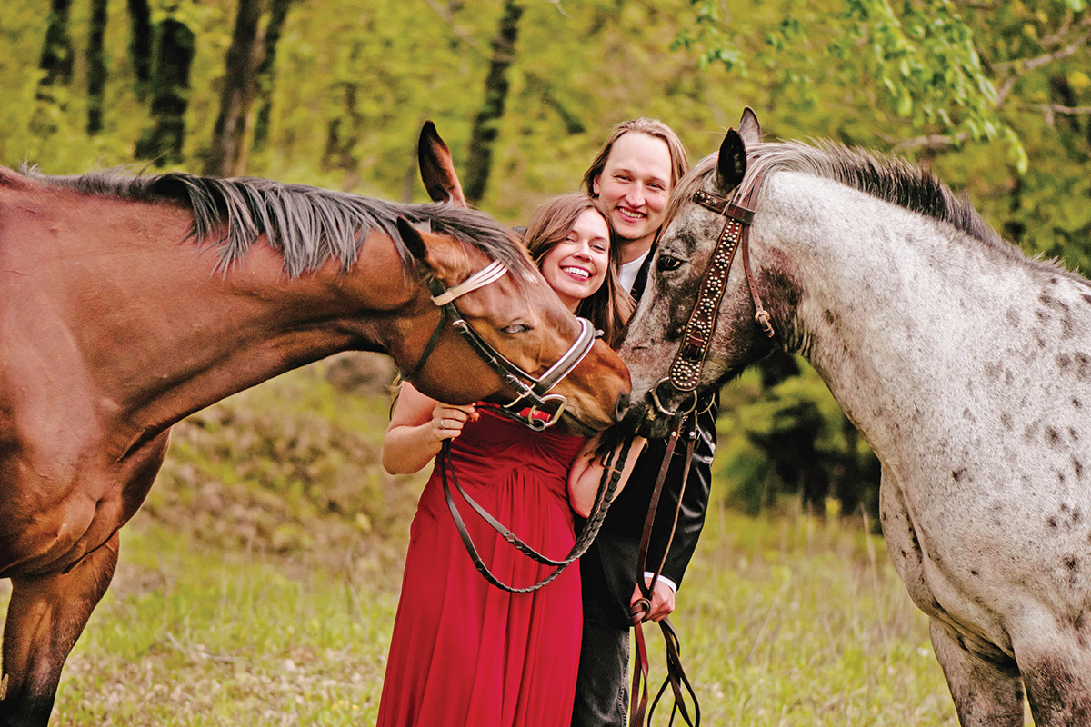 An engagement photo of a couple with two horses