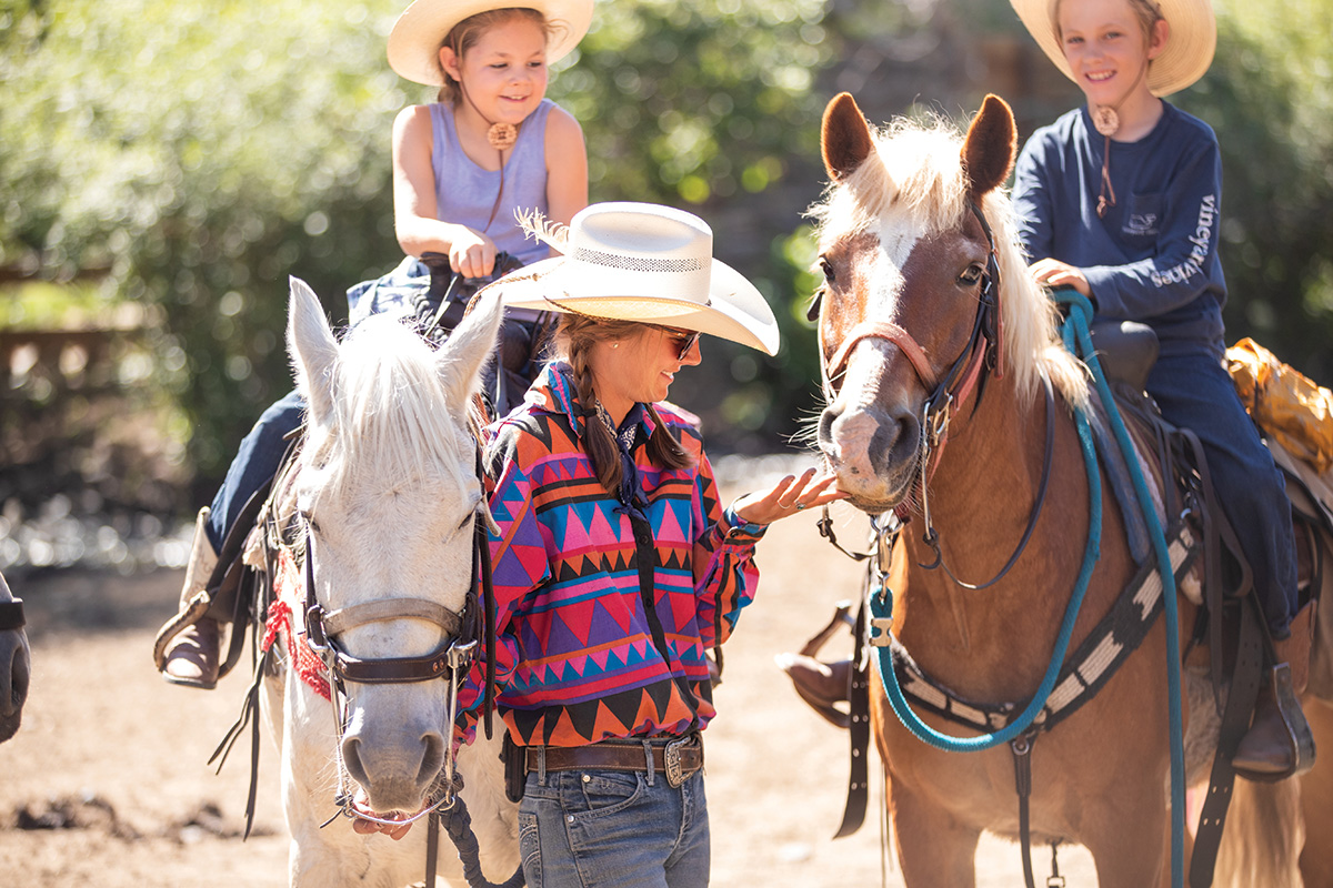 A trail guide at a dude ranch gets two guests situated on their horses