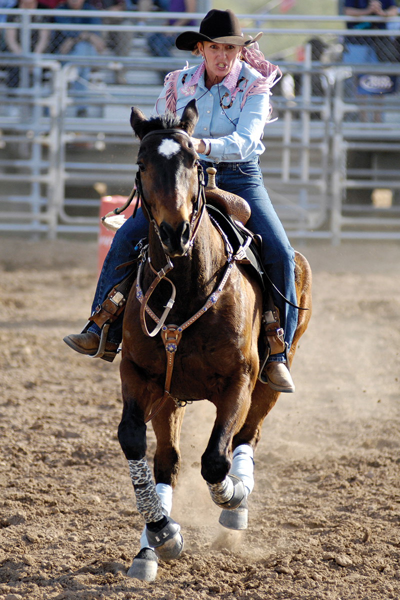 A barrel racer and her horse gallop back.