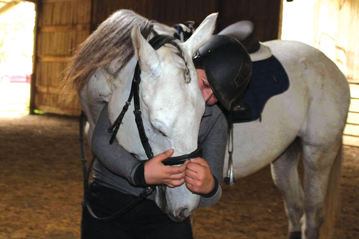 An equestrian hugs her gray horse.