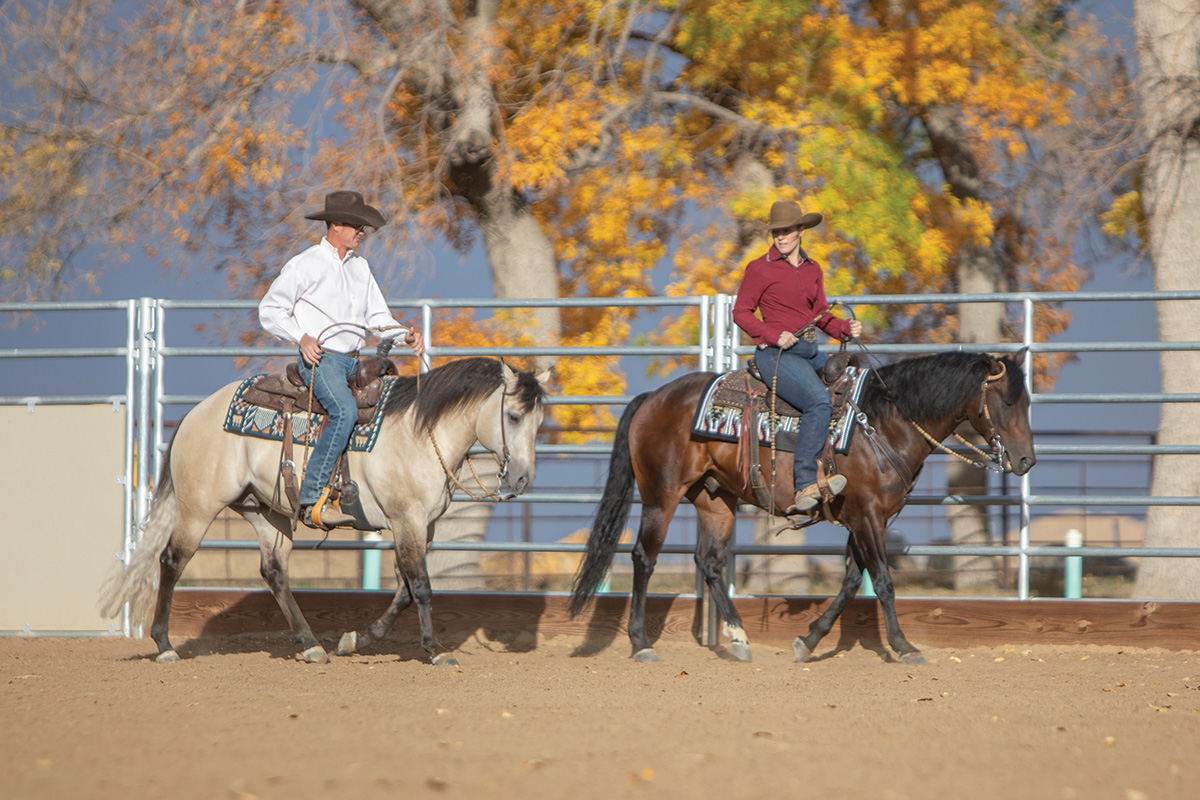 Two western riders riding their horses along a fenceline