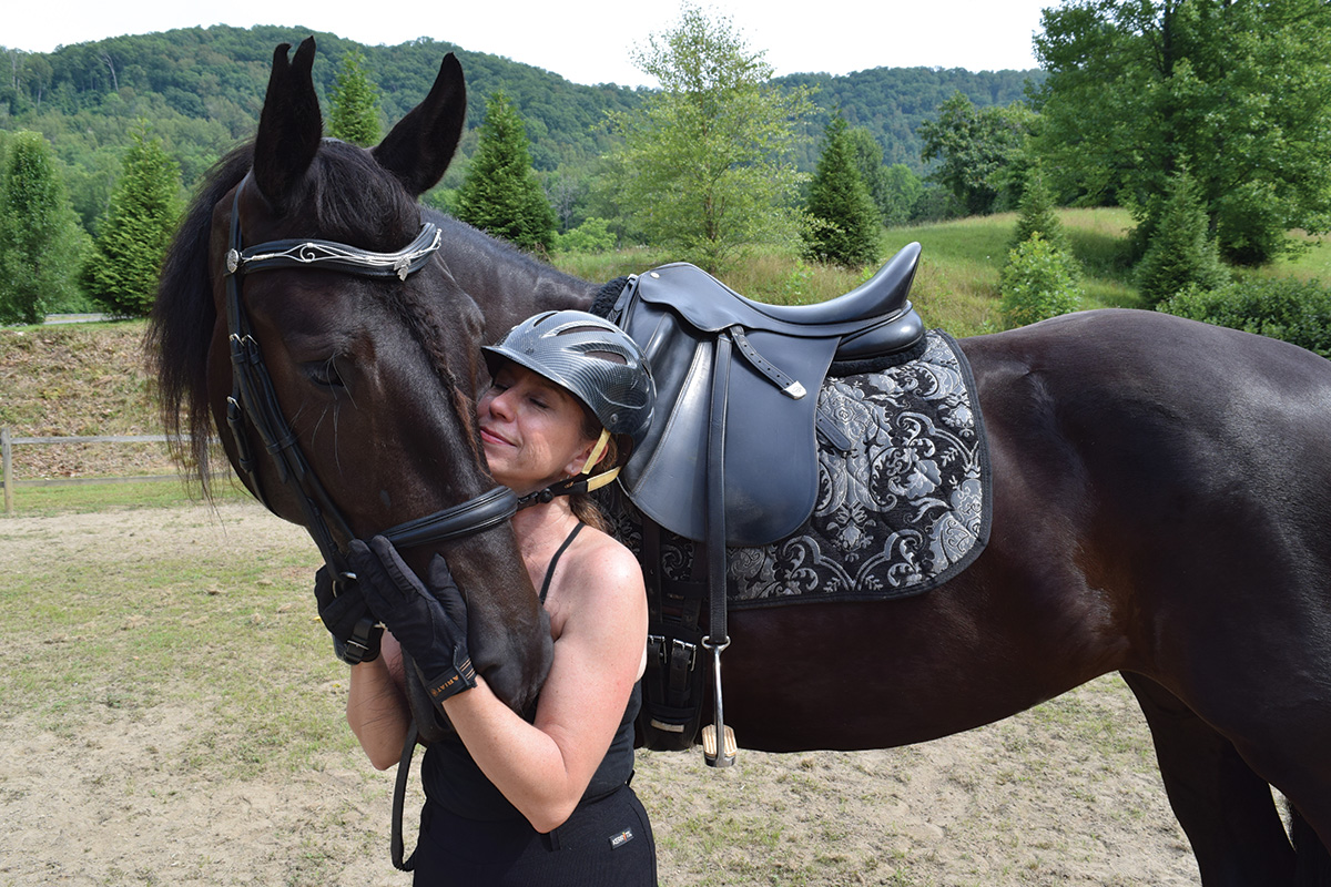 A woman cuddles a black horse in dressage tack