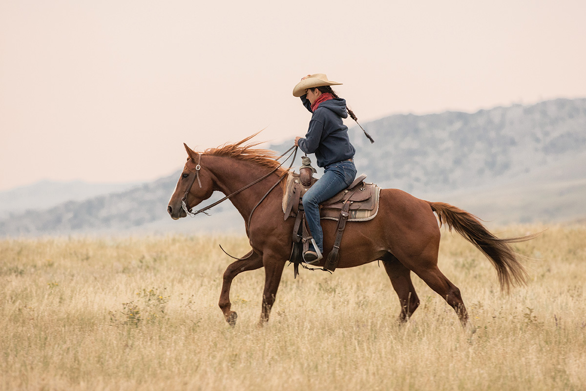 A cowgirl rides across the valley in the foothills