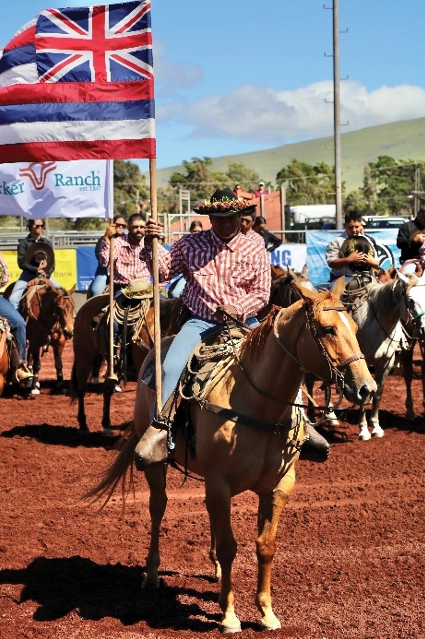 A paniolo holds the state flag of Hawaii at a rodeo.