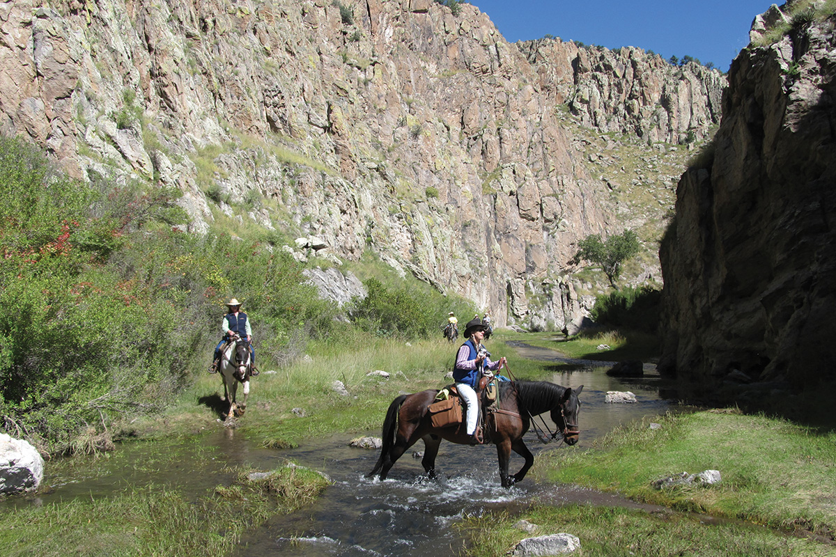Guests at a dude ranch ride their horses through a river canyon