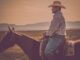 A cowboy overlooks a ranch with a mountain backdrop