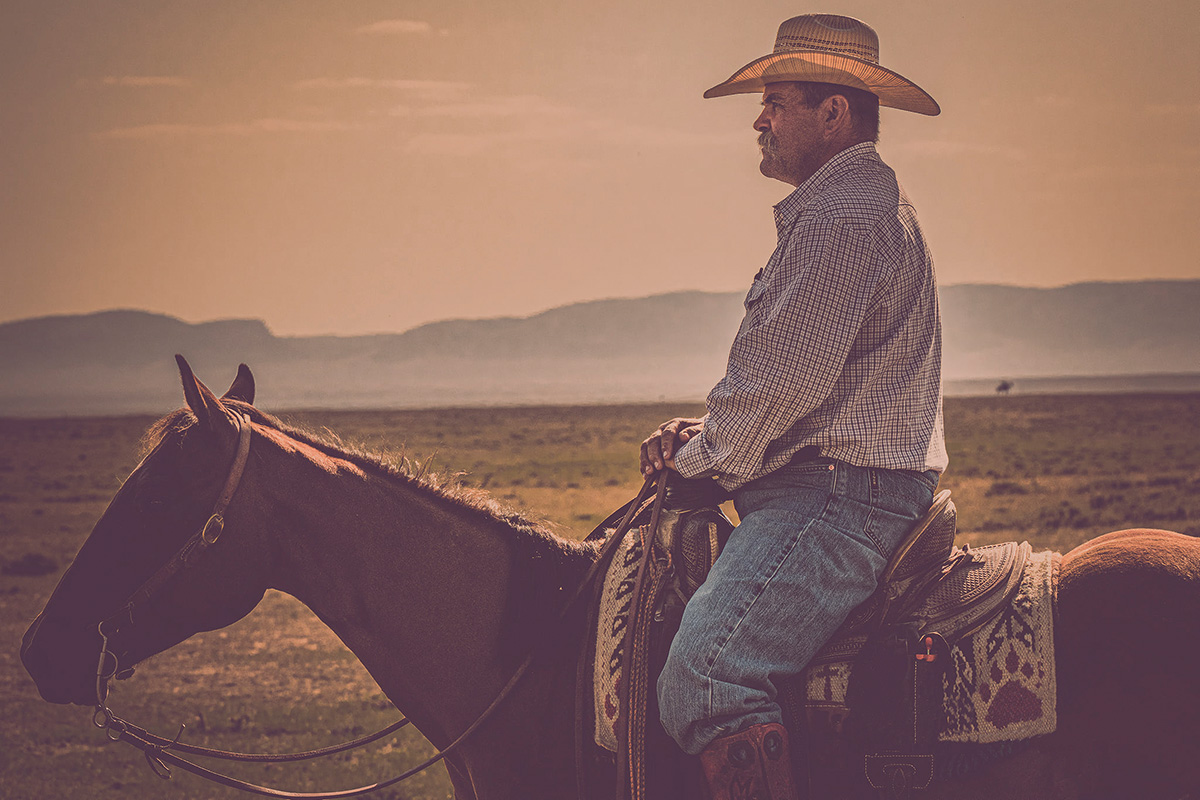 A cowboy overlooks a ranch with a mountain backdrop