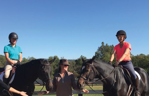 Riders with animal communicator standing between two horses.
