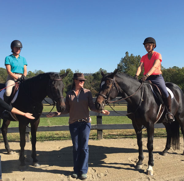 Riders with animal communicator standing between two horses.