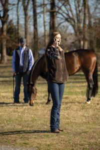 Woman calling virtual veterinarian while standing near horse.